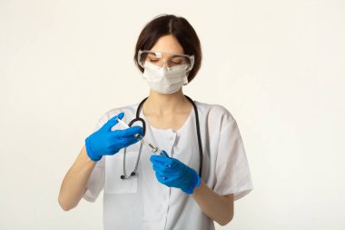 Aşısı ve şırıngası olan beyaz bir arka planda tıbbi giysili genç bir kadın.