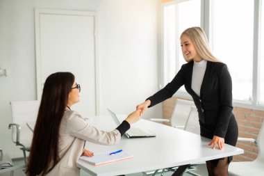 Ofiste takım elbiseli iki güzel genç kadın el sıkışıyor. 