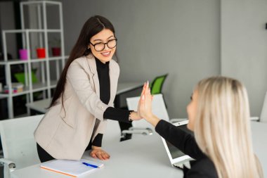 Ofiste takım elbiseli iki güzel genç kadın el sıkışıyor. 