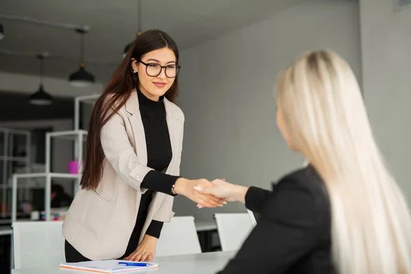 Ofiste takım elbiseli iki güzel genç kadın el sıkışıyor. 