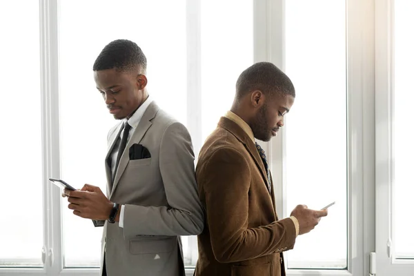 two handsome african men in suits at the office with mobile phones