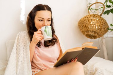 beautiful young woman in the bedroom on the bed with a book and a cup of tea 