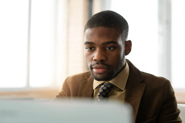 handsome young african man in suit at table in office with laptop