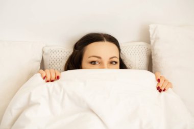 Güzel genç bayan yorganın altında yatar. 