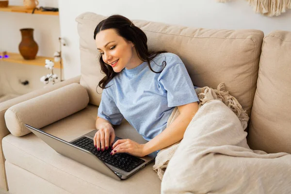 beautiful young woman in pajamas lies at home on the couch with a laptop