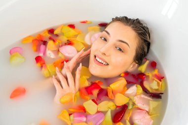 Güzel genç bir kadın gül yapraklarıyla banyo yapıyor.