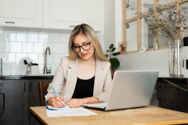 Evde dizüstü bilgisayarla çalışan güzel genç bir kadın.