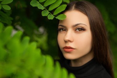 Yeşil yaprakların yanında güzel bir kadın makyajı olan nazik bir görüntü.