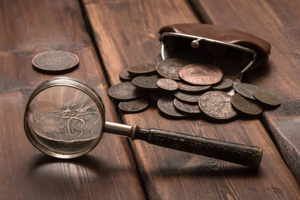 Old ancient coins and magnifying glass on the brown wooden table background