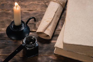 Kalem, mürekkep hokkası, parşömen tomarı, kitaplar ve yanan mum..