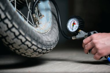 Bir işçi arabanın lastiğinin yanındaki motosiklet tekerleğini şişiriyor. Silahı şişiriyor..