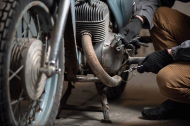 Elinde İngiliz anahtarı olan bir tamirci kırık motorsiklet arka planında oturuyor. Motosiklet tamir hizmeti kavramı.
