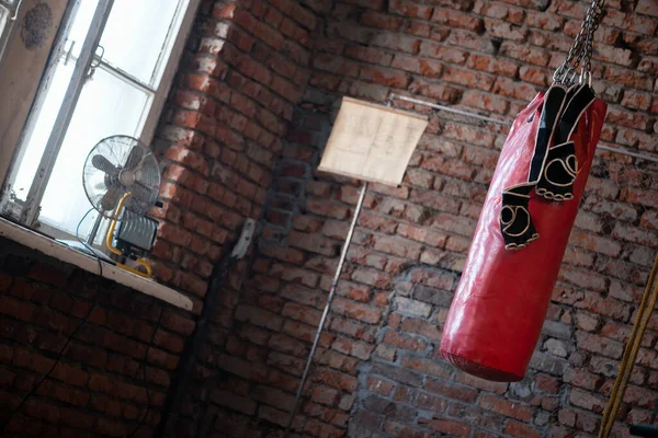 Old punching bag and boxing gloves on the brick wall background.