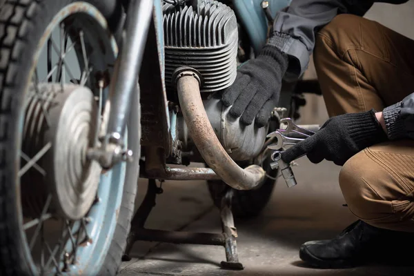 A mechanic with a wrenches in hand is sitting on the broken motorbike background. Motorcycle repairing service concept.