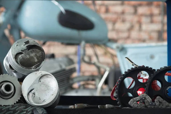 Motorcycle repairing service concept background. A car engine piston, gear and wrenches on the rack on the old garage background.