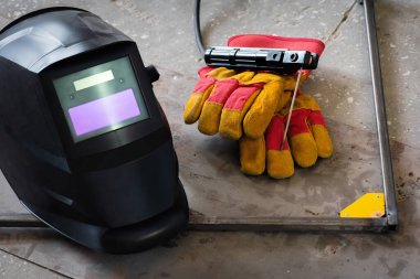 Kaynak başlığı, eldivenler ve zeminde metal çerçeve..