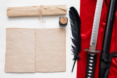 Katana kılıcı, beyaz tahta masa zemininde kopya alanı ve antik kağıt parşömeni olan boş bir sayfa kitabı. Dövüş teknikleri kitabı konsepti.