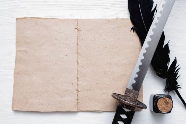 Katana kılıcı, beyaz tahta masa zemininde kopya alanı ve antik kağıt parşömeni olan boş bir sayfa kitabı. Dövüş teknikleri kitabı konsepti.