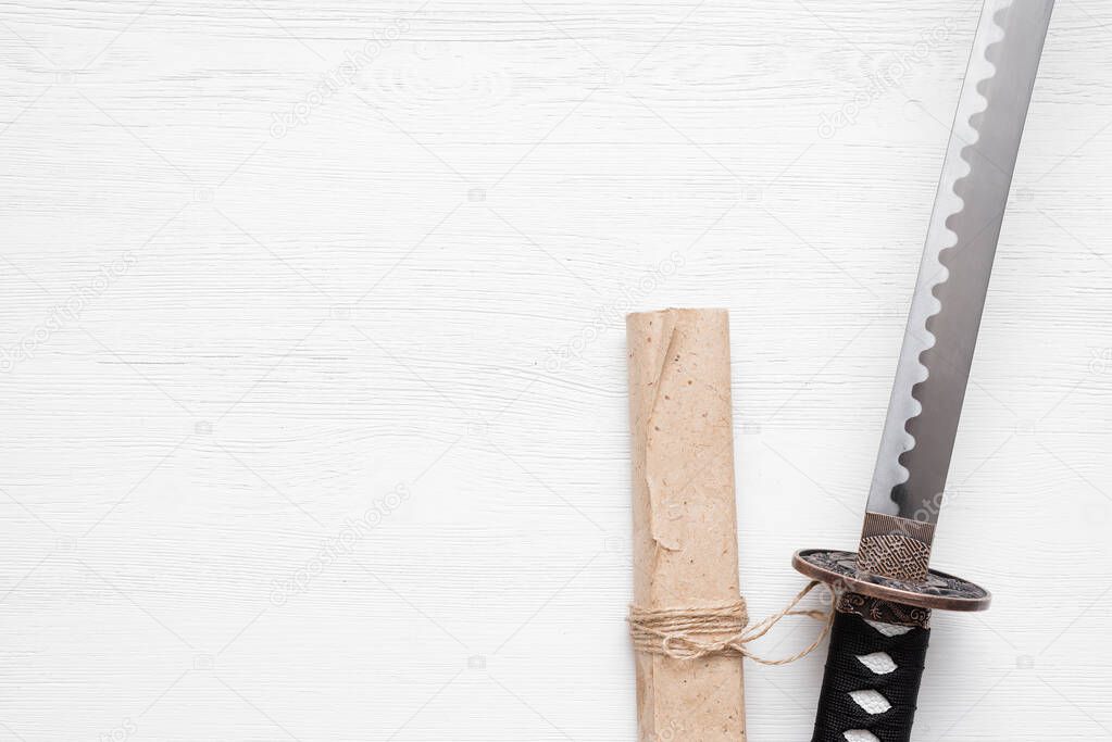 Katana sword and ancient paper scroll on the white wooden table background with copy space.