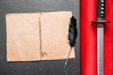 Samuray masal kitabı taslağı. Katana kılıcı kırmızı kumaşta ve boş sayfa kitabı. Masada kopya alanı var..