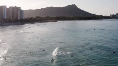 Okyanusun üzerinde geriye doğru uçmak ve Waikiki Sahili 'nde sörfçüler. Arkaplan olarak ünlü Diamond Head krateri. Gün doğumunda sabah ışığı