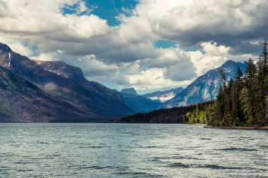 Güneşli yaz gününde, Buzul Ulusal Parkı 'nda Sherburne Gölü. Mavi gökyüzünde beyaz dramatik bulutlar.