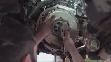 Bir tamirci atölyede araba debriyajı montajı yapıyor.