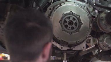 Bir tamirci atölyede araba debriyajı montajı yapıyor.