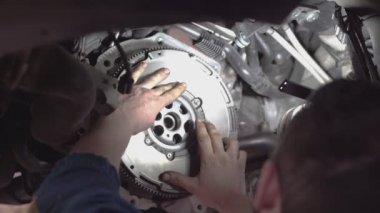 Bir tamirci atölyede araba debriyajı montajı yapıyor.