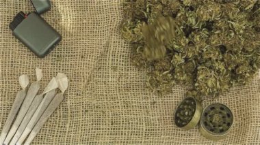 Öğütücüyle marihuana, sarmalar ve yukarıdan yavaş çekimde düşen yabani ot çiçekleri.