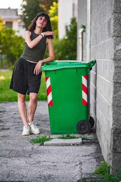 Cute Brunette girl near garbage dumpster outdoor