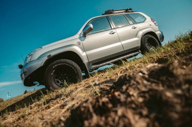 Rome, italy 10 september 2025: silver suv off-road vehicle driving up a steep grassy hill against a clear blue sky, showing adventure and extreme travel concept