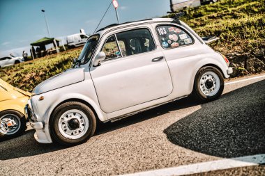 Rome, italy 10 september 2025: custom white fiat 500 vintage rally car with race stickers and spoilers parked on sunlit asphalt at outdoor car show event