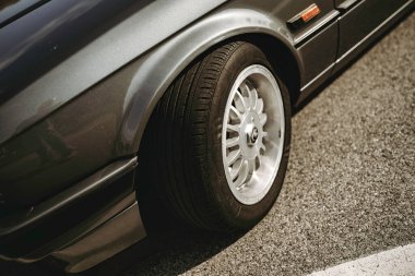 Rome, italy 10 september 2025: vintage bmw e30 sedan side detail showing wheel, tire, fender and bodywork parked on sunlit asphalt, classic automotive styling