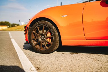Rome, italy 10 september 2025: orange mazda miata wheel and fender close-up on sunlit asphalt with road marking, low-angle detail of sporty performance car