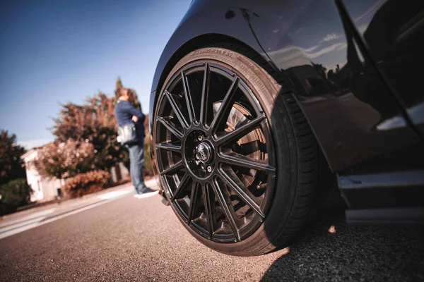 Rome, italy 10 september 2025: black sports car wheel and tire on asphalt, low-angle detail shot with person blurred in background under clear blue sky, modern automotive design