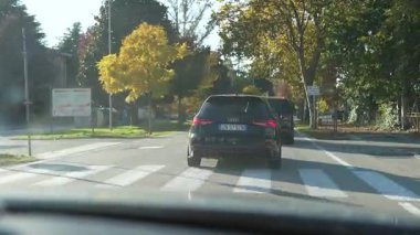 Roma, 27 Ekim 2025: güneşli bir sonbahar gününde siyah bir spor arabayı takip eden sürücünün bakış açısı. Şehir renkli ağaçlarla asfalt bir yolda ilerliyor.