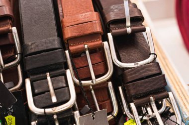 Parlak metal tokalı ve fiyat etiketli çeşitli hakiki deri kemerlerin yakın plan görüntüsü, erkek ve kadınlar için zanaat, stil ve moda seçenekleri vurgulanıyor