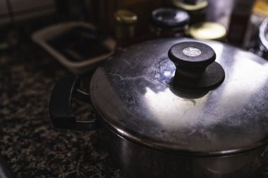 Kapağı benekli mutfak tezgahına kapatılmış paslanmaz çelik tencere, ev yapımı bir yemeği pişirmeye ya da sıcak tutmaya hazır; günlük mutfak malzemesi ve yüzey dokusuna yakın çekim
