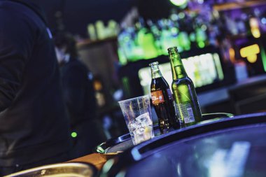 Este, İtalya 28 Ekim 2025: neon ışıklı bir barda serinletici içecekler, buzlu bardaklar ve şişelerle dolu canlı bir gece sahnesi, şenlikli sosyal atmosfer.