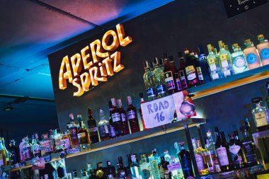 Este, İtalya 28 Ekim 2025: Parlak aperol spreyli neon levhalı bar içi çeşitli içki şişeleri raflarının üzerinde, şık bir gece barı ambiyansı.