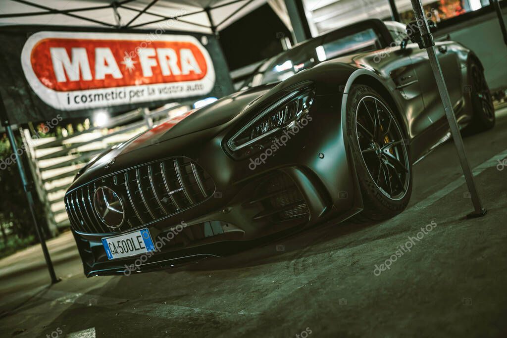 Este, italy 28 october 2025: mercedes-amg gt c roadster in matte black at a night car show with ma-fra banner, reflections, low-angle view, premium performance image.