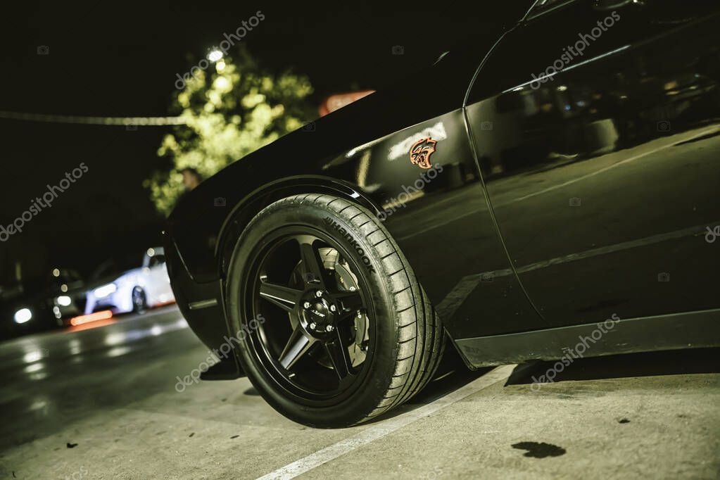 Este, italy 28 october 2025: black dodge challenger hellcat wheel and fender close-up at night in a parking lot, glossy muscle car detail and emblem lighting