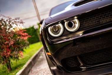 Siyah Dodge meydan okuyucusu aydınlanmış ön farlarını ve agresif ön ızgarasını sergiliyor. Açık hava ortamında güç, performans ve modern otomotiv tasarımını yansıtıyor.