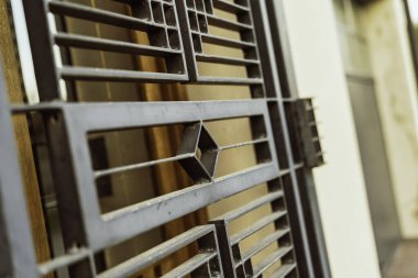 Metal kapı parmaklıkları, sıcak, güneşli bir arka plana karşı tekrarlanan elmas ve dikdörtgen geometrik deseni içerir, güvenlik ve mimari tasarımı temsil eder.