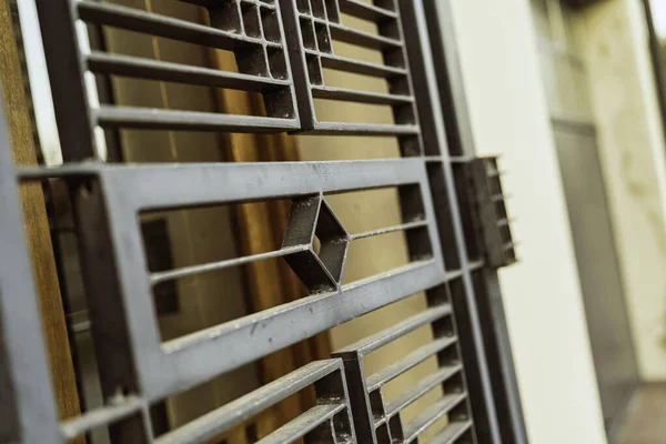 Metal kapı parmaklıkları, sıcak, güneşli bir arka plana karşı tekrarlanan elmas ve dikdörtgen geometrik deseni içerir, güvenlik ve mimari tasarımı temsil eder.