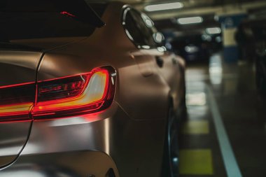 Milan, İtalya, 28 Ekim 2025: modern araba arka profili aydınlatılmış arka lambayı ortaya çıkarıyor, karanlık bir yeraltı garajına park edilmiş, arka farı bulanık.