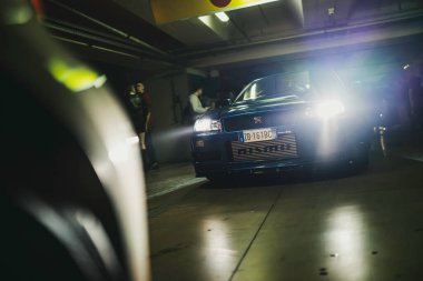 Milano, İtalya, 28 Ekim 2025: İnsanlar yeraltı otoparkındaki parlak farlı mavi Nissan Skyline gt-r34 spor arabaya hayran.