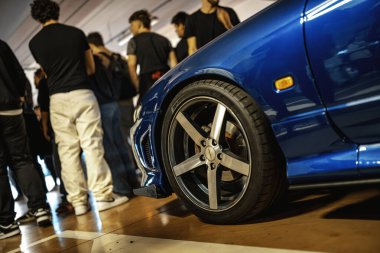 Milan, İtalya, 28 Ekim 2025: Kalabalık kapalı bir otomobil fuarında krom alaşım tekerleği ve lastiği cilalayan özel mavi spor arabalara hayran, yakın çekim detayı.