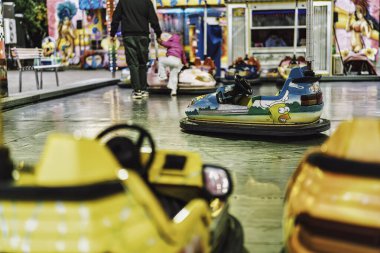 Milan, İtalya 27 Ekim 2025: Parlak bir fuar alanında parlak bir pistte dizilmiş renkli çarpışan arabalar, insanlar güneşli karnaval atmosferinde geziniyor ve eğleniyorlar.